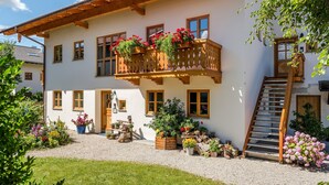A traditional chalet with a wooden balcony, a gravel driveway, and a staircase leading to the entrance. - Holiday Apartment “Beim Paulfischer - Eckbankerl” Close to Chiemsee with Balcony & Terrace (Chieming)