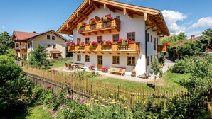 A traditional chalet with a wooden balcony, a garden, and a wooden fence. - Holiday Apartment “Beim Paulfischer - Eckbankerl” Close to Chiemsee with Balcony & Terrace (Chieming)