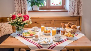 A breakfast table with a variety of food items, a vase of flowers, and a window with curtains. - Holiday Apartment “Beim Paulfischer - Eckbankerl” Close to Chiemsee with Balcony & Terrace (Chieming)