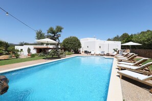 A swimming pool with lounge chairs, a picnic table, and a white building in the background. - Heavenly Villa "Can Caseres" with Saltwater Pool, Orchard and Mountain View (Santa Eulalia del Rio)