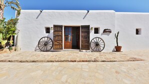 Un edificio blanco con puerta de madera, dos ruedas de madera y una planta en maceta.