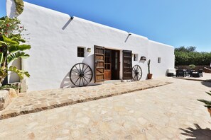 A white building with a stone-paved entrance, wooden doors, and large wheels on the side. - Heavenly Villa "Can Caseres" with Saltwater Pool, Orchard and Mountain View (Santa Eulalia del Rio)