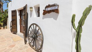 Un edificio blanco con puerta de madera, un letrero de madera que dice 'CAN CASERES' y un gran carruaje de rueda.