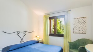 Une chambre à coucher comprenant un lit, une chaise, une petite table, une fenêtre avec des rideaux et un élément de décoration murale.