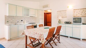 Une cuisine de taille réduite comprenant une table à manger, des chaises, une cuisinière et un téléviseur.