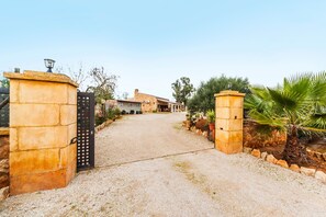 Un cancello con un vialetto sterrato che conduce a un edificio con facciata in pietra e tetto a tegole.