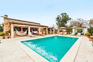 Un'area piscina con un edificio in pietra, poltrone a sdraio e ombrelloni.