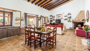 A spacious dining area with a wooden table and chairs, a kitchen with a tiled backsplash, and a fireplace. - Embedded in Nature and with Pool - Finca Esplendor (CAMPOS)