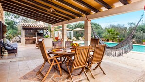An outdoor patio with a wooden table and chairs, a hammock, and a pool. - Embedded in Nature and with Pool - Finca Esplendor (CAMPOS)