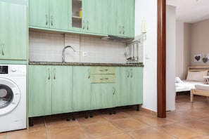Una cucina con mobili verdi, lavatrice integrata e zona pranzo con un letto.