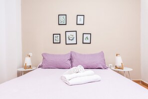 A neatly made bed with two pillows, a folded towel, and a bedside lamp on a white nightstand.