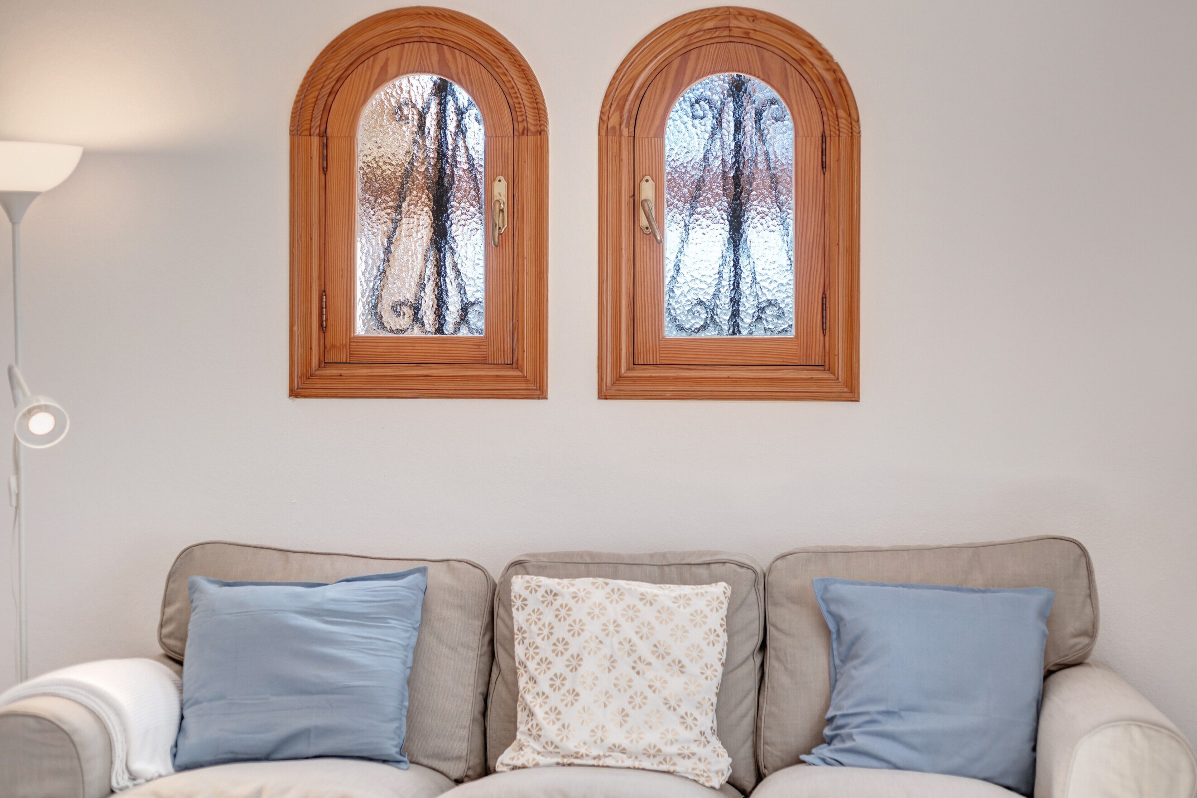 A room with a sofa, two arched windows, and a lamp.