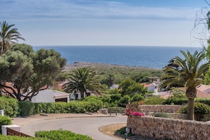 A coastal residential area with a curved road, stone walls, and houses with red-tiled roofs.