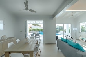 A modern interior with a dining area, a sofa, and a view of a swimming pool.