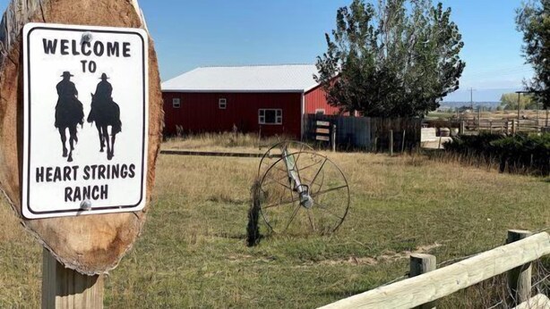 A welcome sign for Heart Strings Ranch with a red barn and a wooden fence in the background. - Heart Strings Ranch- Views of Heart Mountain & Near Horses! (Cody)