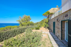 Un bâtiment en pierre doté d’un balcon, un jardin avec différentes espèces de plantes et une vue sur la mer.