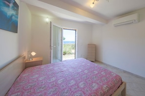 Une chambre à coucher comprenant un lit, une table de chevet, une commode et une porte ouverte donnant sur un balcon.