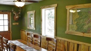 A dining area with a wooden table and chairs, a mounted deer head, a window, and a map on the wall.