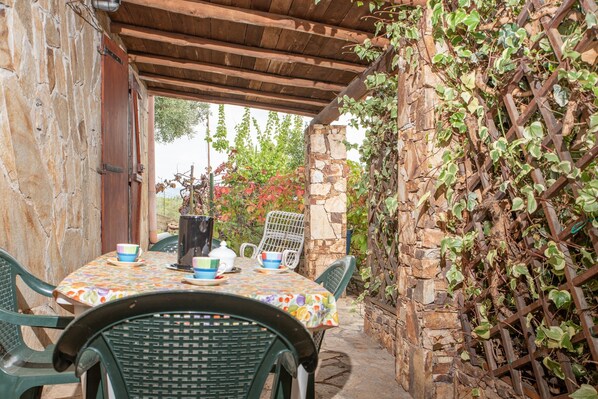 Un patio al aire libre con una mesa para dos, rodeado de muros de piedra y vegetación.