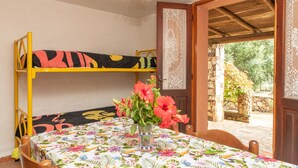 Een kamer met stapelbedden, een tafel met een tafelkleed met bloemenmotief, en een vaas met bloemen.