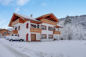 Un chalet à plusieurs étages doté de balcons, de grandes fenêtres et d’une allée enneigée.