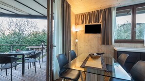 A modern dining area with a glass table, black chairs, and a wooden deck. - Idyllic and with spectacular mountain views – Apartment GeoResort C10 (Tremosine)