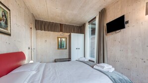 A hotel room with a large bed, a television mounted on the wall, a wardrobe, and a window with curtains. - Idyllic and with spectacular mountain views – Apartment GeoResort C10 (Tremosine)