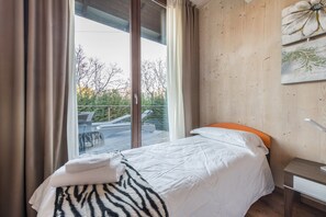 Une chambre à coucher comprenant un lit, une table de chevet, une fenêtre avec des rideaux et une vue sur des meubles d’extérieur.