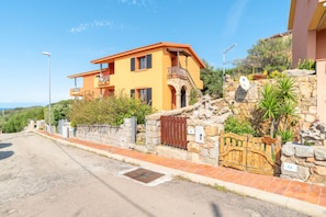 A two-story building with a stone wall and a wooden gate, a clear sky, and a road in the foreground.