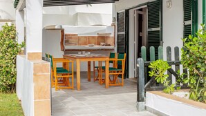 Eine Terrasse im Freien mit Tisch, Stühlen, einem Grill und einem überdachten Bereich.