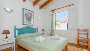 Ein Schlafzimmer mit einem Bett, zwei Nachttischen, einem Sessel, einem Fenster und einem Wandbild.