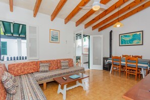 Quarto com sofá, mesa, mesa de jantar com cadeiras, vigas de madeira no teto e um quadro na parede.
