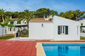 Um edifício branco com piscina, venezianas verdes e telhado em telhas.