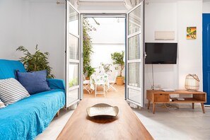 An open-plan living area with a sofa, a wooden coffee table, a TV, and a dining table with chairs.