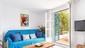 Un salon lumineux avec un canapé bleu, une table basse en bois, un tableau accroché au mur et une porte-fenêtre coulissante donnant sur un espace extérieur.