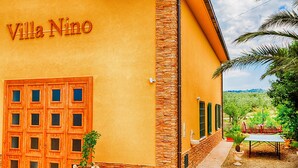 En bygning med skiltet 'Villa Nino', en trædør med glasruder og et lille udendørs siddeområde med et bord og stole.
