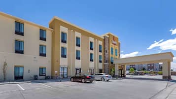 Hotel Comfort Suites com estacionamento, dois carros estacionados e um céu azul claro.