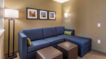 Ein modernes Hotelzimmer mit einem Ecksofa, zwei Hocker, einer Stehlampe und drei gerahmten Bildern an der Wand.