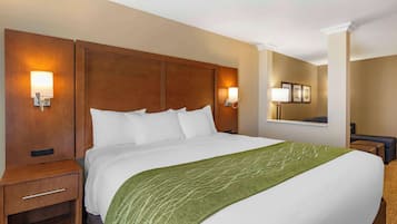 A hotel room with a large bed, wooden headboard, bedside lamps, a green throw blanket, and a small nightstand.