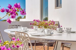 A dining table set with white plates, cups, and glasses, surrounded by chairs with a geometric design. - Air-Conditioned Villa with Sea View, Pool, Jacuzzi, Rooftop Gym/Terrace & Wi-Fi (Costa De La Calma, CALVIÀ)