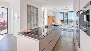 A modern kitchen with a central island, a dining area with white chairs, and a view of the outdoors. - Air-Conditioned Villa with Sea View, Pool, Jacuzzi, Rooftop Gym/Terrace & Wi-Fi (Costa De La Calma, CALVIÀ)
