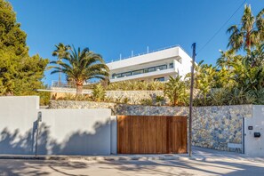 A modern building with a stone wall, a wooden gate, and a clear blue sky. - Air-Conditioned Villa with Sea View, Pool, Jacuzzi, Rooftop Gym/Terrace & Wi-Fi (Costa De La Calma, CALVIÀ)