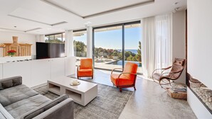 A modern living room with a sofa, two armchairs, a coffee table, a flat-screen TV, and a large window with a view of the ocean. - Air-Conditioned Villa with Sea View, Pool, Jacuzzi, Rooftop Gym/Terrace & Wi-Fi (Costa De La Calma, CALVIÀ)