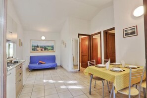 A compact kitchen with a stove, a blue sofa, a dining table set for two, and a painting on the wall.