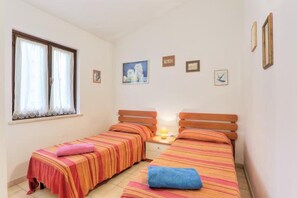 Une chambre avec deux lits, une fenêtre avec des rideaux et plusieurs tableaux encadrés accrochés au mur.