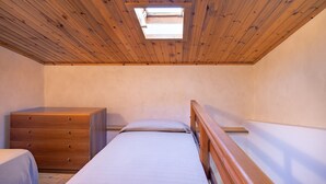 Una habitación pequeña con cama individual, techo de madera, cómoda y tragaluz.