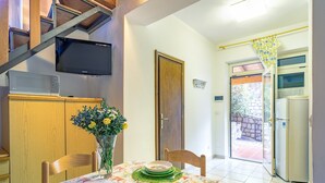 Un comedor con una mesa dispuesta para cuatro, un televisor montado en la pared y una puerta que da a un espacio exterior.