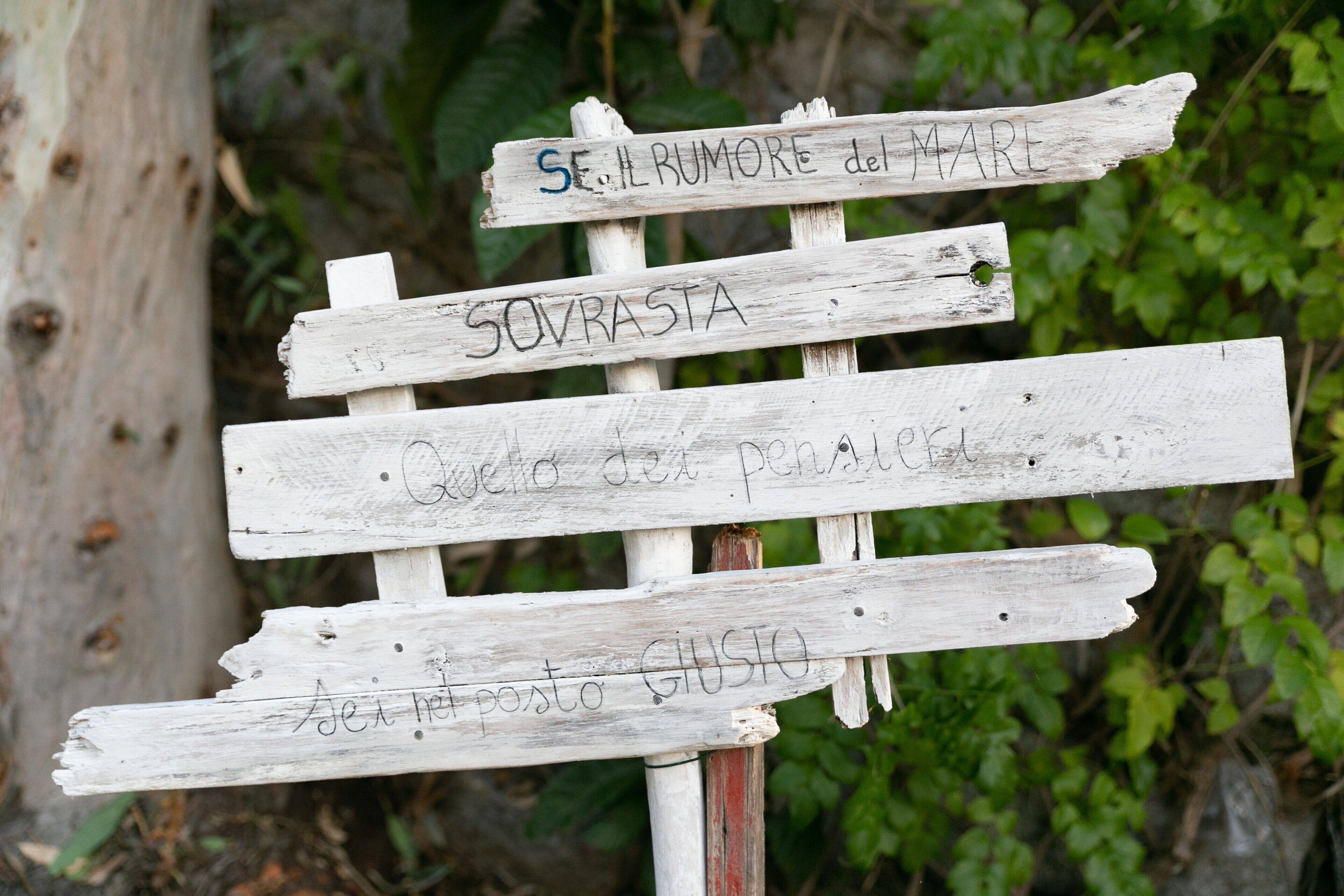Un panneau indicateur en bois rustique, sur lequel figurent des indications manuscrites en italien.