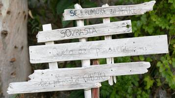 Un panneau indicateur en bois rustique, sur lequel figurent des indications manuscrites en italien.