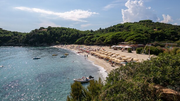 Una playa costera con barcos, sombrillas y sillas de playa.